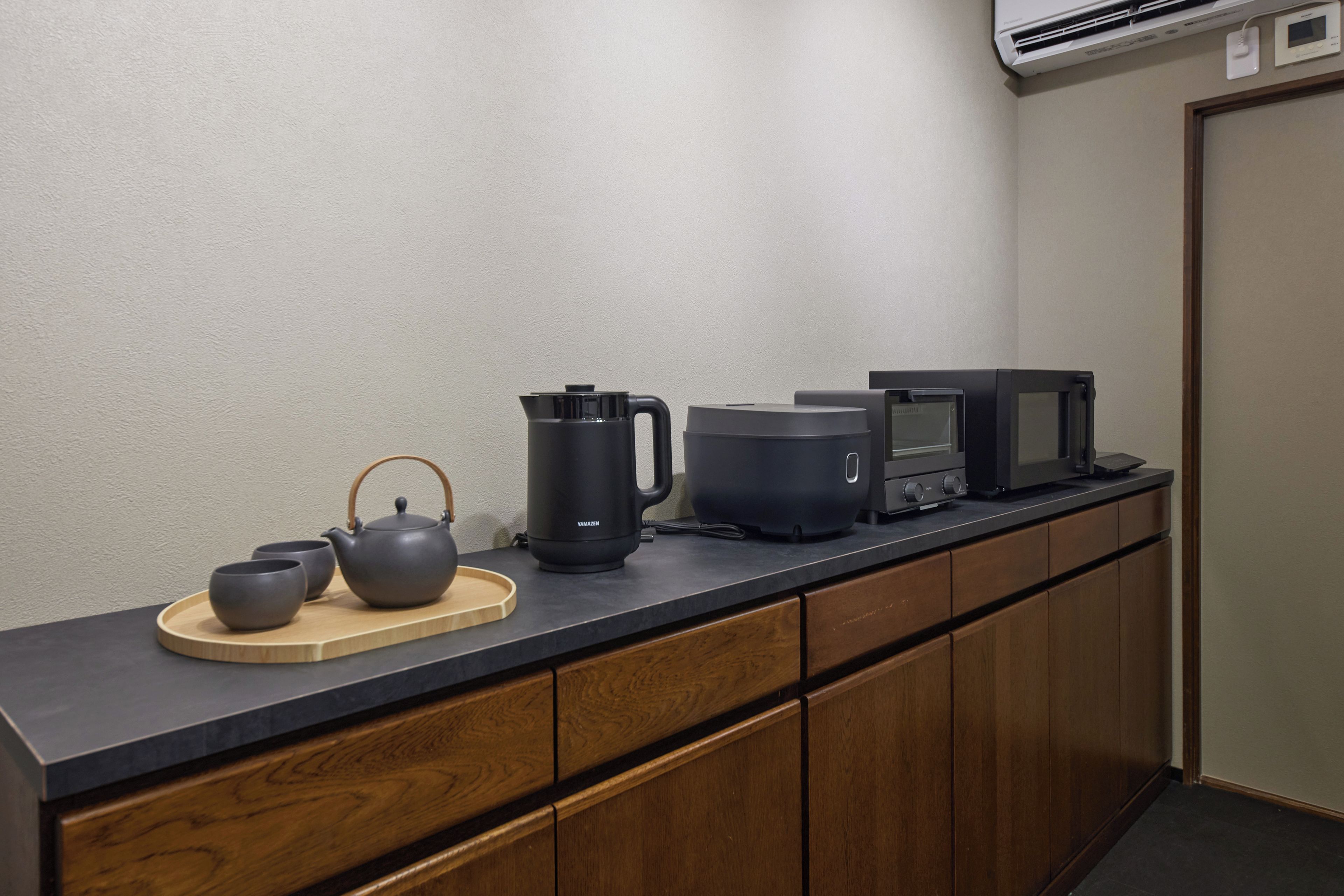 A kitchen with a black countertop, a teapot, a kettle, and a microwave.