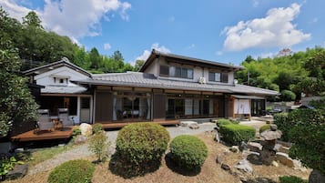 A traditional Japanese-style building with a wooden deck, large windows, and a garden with rocks and shrubs.