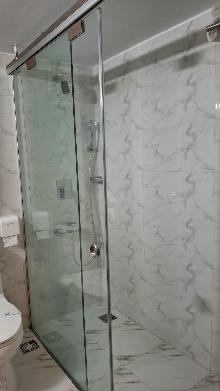 A glass-enclosed shower with a marble-tiled wall.