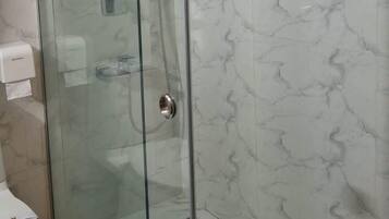 A glass-enclosed shower with a marble-tiled wall.