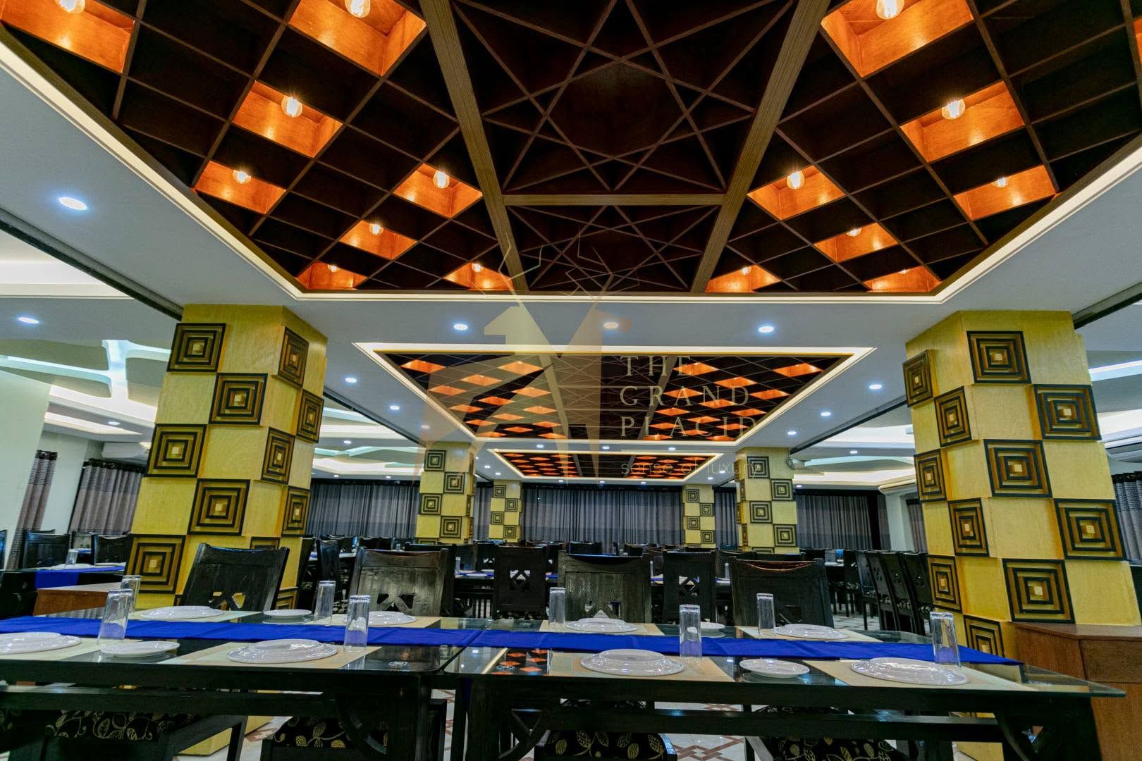 Une salle de conférence avec des tables disposées pour une réunion, un plafond orné de motifs et un panneau indiquant « THE GRAND PLACE ».