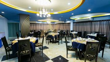 A hotel dining area with multiple tables, chairs, and a modern chandelier.