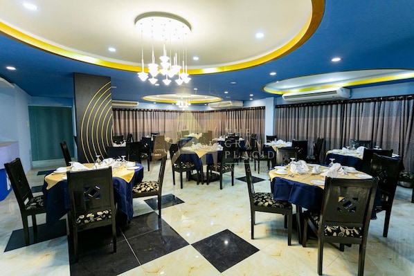 A hotel dining area with multiple tables, chairs, and a modern chandelier.