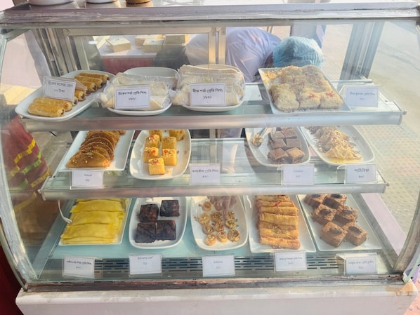 A display case with various baked goods and desserts, including pastries and cakes, each labeled with their name and price.