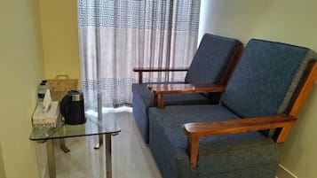 Un salón con sofá, dos sillas de madera, una mesa de vidrio, un hervidor y una cesta.