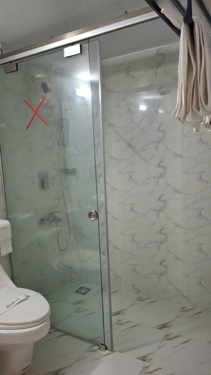 A bathroom with a glass shower enclosure, a toilet, and a towel hanging on a rack.