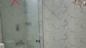 A bathroom with a glass shower enclosure, a toilet, and a towel hanging on a rack.
