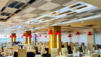 A spacious dining area with multiple tables and chairs, a patterned floor, and a ceiling with a geometric design.