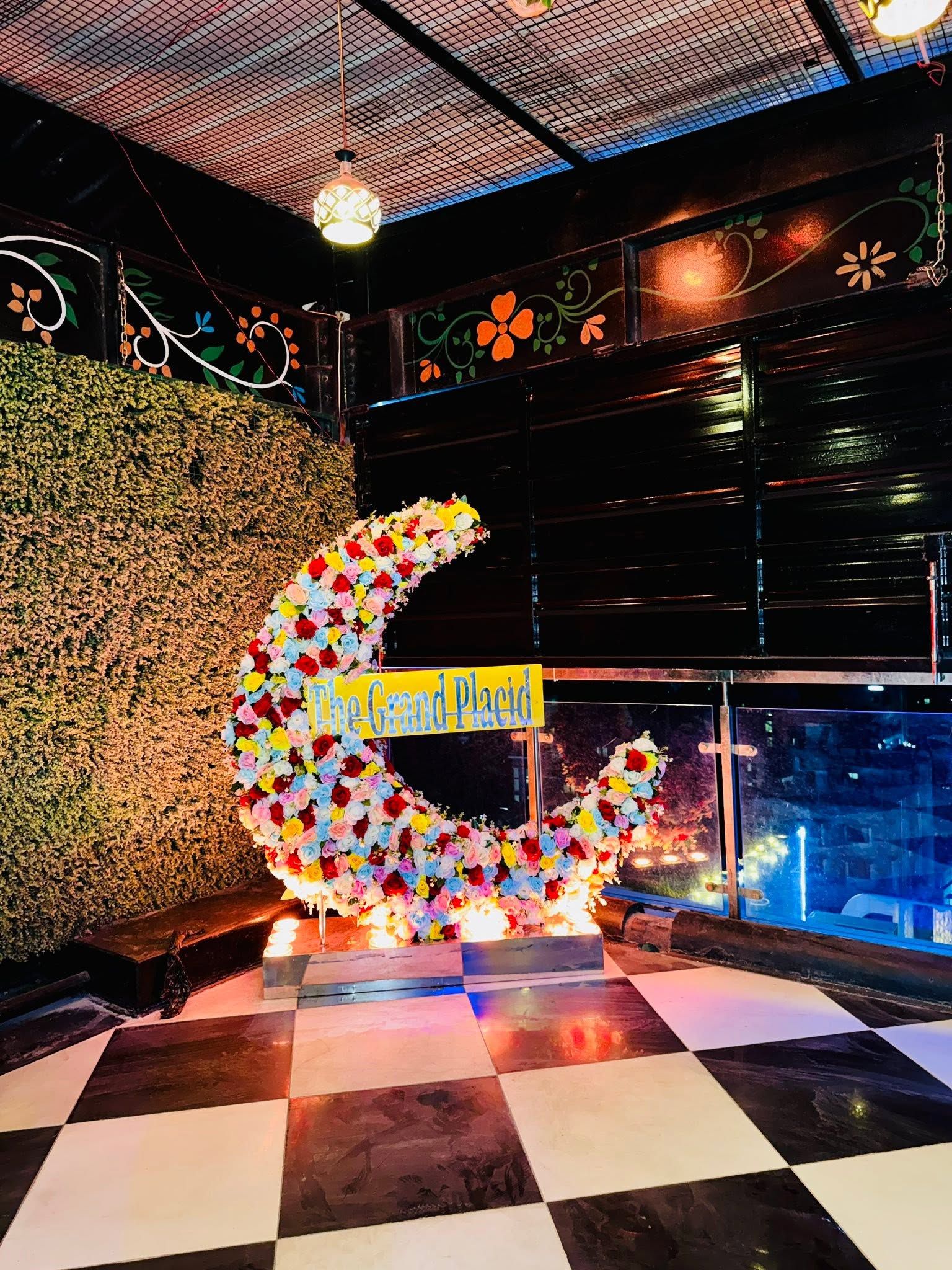 A decorative crescent made of flowers with a sign reading 'The Grand Place.'