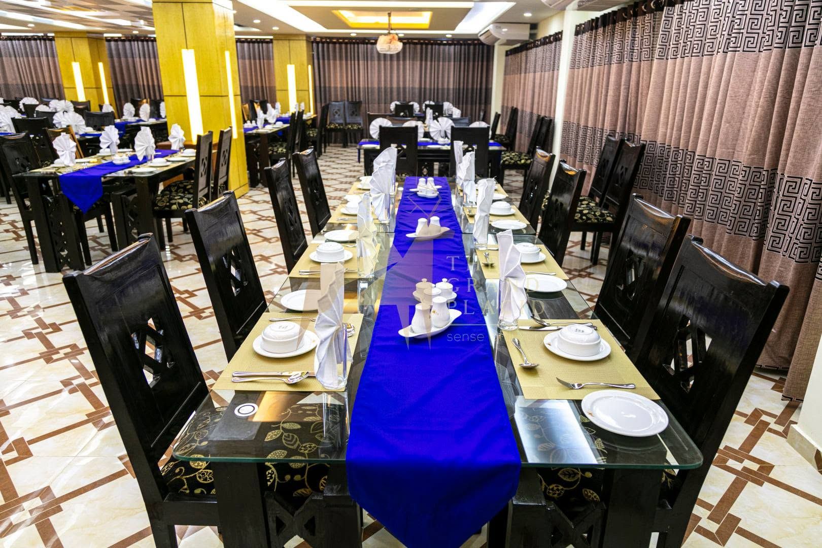 A banquet hall with long tables set for a formal event, featuring black chairs, blue tablecloths, and white table settings.