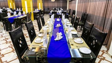 A banquet hall with long tables set for a formal event, featuring black chairs, blue tablecloths, and white table settings.