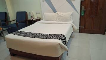 A hotel room with a bed, a chair, a nightstand, a lamp, and a door.