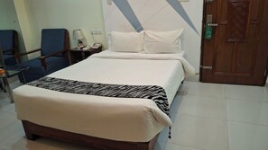 Una habitación de hotel con cama, una silla, mesita de noche, lámpara y puerta.