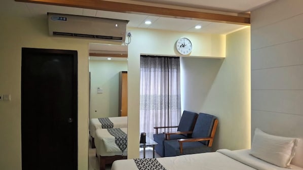 A hotel room with a bed, a chair, a clock, and an air conditioning unit.