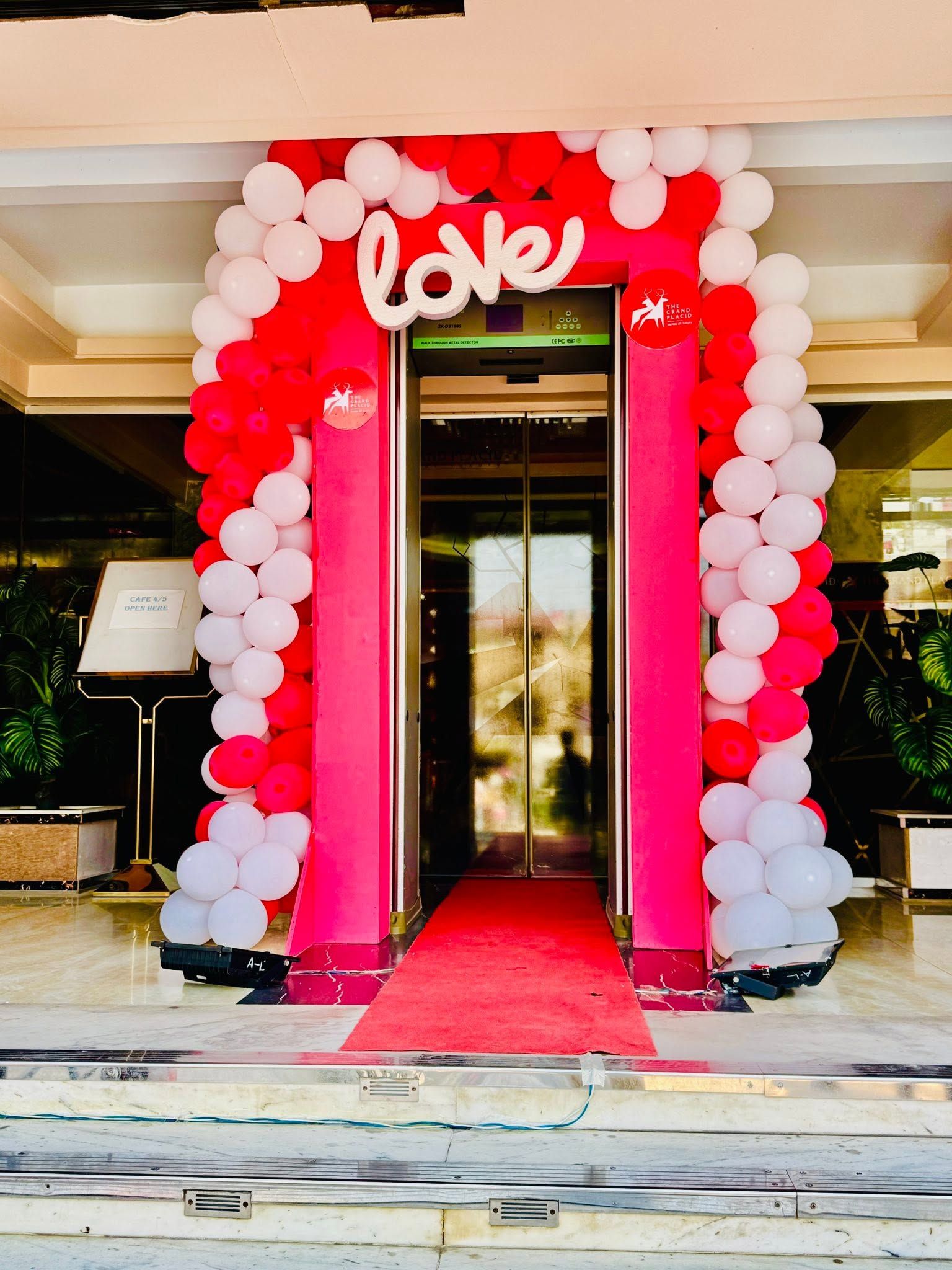 A hotel entrance with a red and white balloon arch and a red carpet leading to the door.