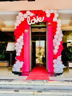 A hotel entrance with a red and white balloon arch and a red carpet leading to the door.