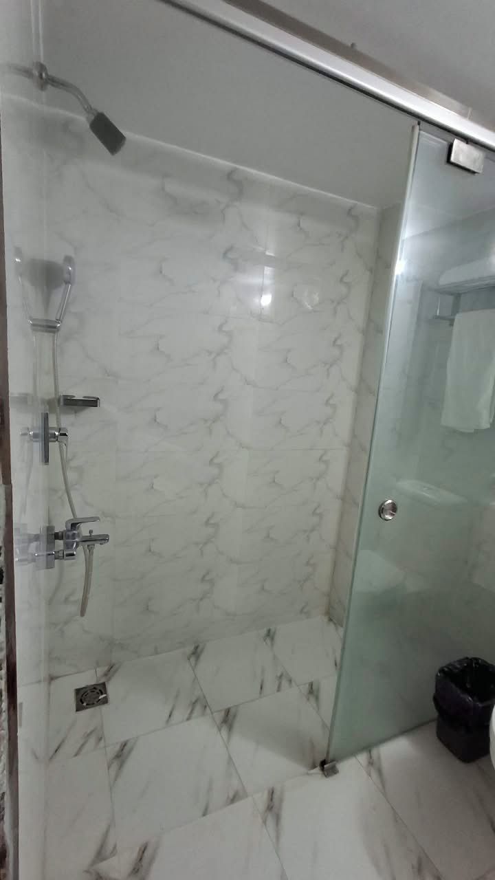 Zona de ducha con paredes de vidrio, piso de mármol y puerta de cristal.