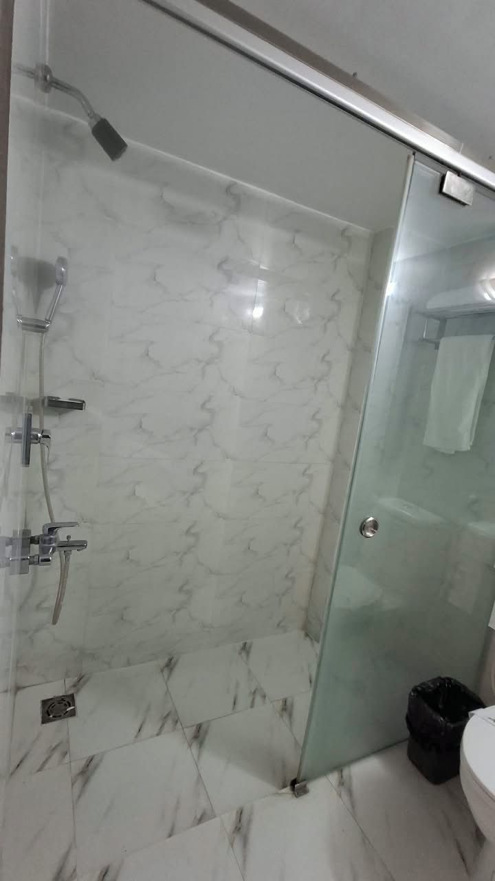 A bathroom with a glass shower enclosure, a toilet, and a trash bin.