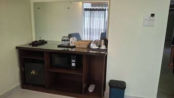 A hotel room with a desk, a trash bin, a microwave, and a small cabinet.