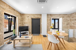 A modern living room with a television, a dining table with chairs, and a stone wall. - Stone Studio with AC | Casa Aldina (Vila Nova de Gaia)