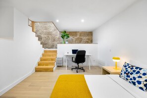 A modern bedroom with a bed, a desk, a chair, a lamp, and a staircase with a stone wall. - Stone Studio with AC | Casa Aldina (Vila Nova de Gaia)