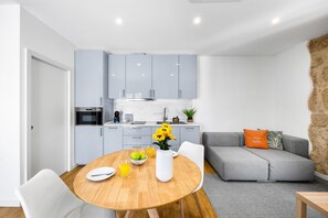 A modern kitchen with grey cabinets, a dining table with a vase of flowers, and a grey sofa with orange pillows. - Stone Studio with AC | Casa Aldina (Vila Nova de Gaia)