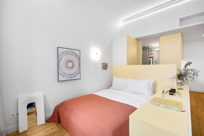 Ein Hotelzimmer mit einem Bett, einem Nachttisch mit Lampe, einem gerahmten Kunstwerk und einer kleinen Pflanze.