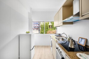 Une cuisine moderne équipée d’un four encastré, d’un évier et d’une fenêtre donnant sur un jardin.