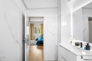 A modern bathroom with a white marble wall, a large mirror, and a sink with a nameplate. - Bright Apartment | Trindade & City Centre (Porto)
