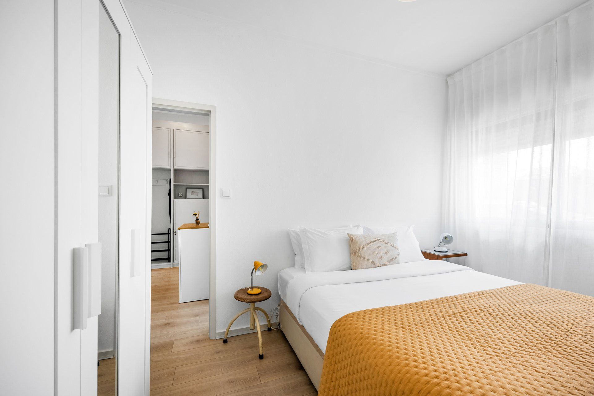 A minimalist bedroom with a bed, bedside table, and a small stool.
