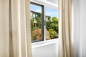 Une fenêtre avec des rideaux, une vue sur la verdure et un bâtiment à l’extérieur.