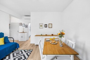 A modern living room with a blue sofa, a wooden dining table with chairs, and a kitchen area in the background. - Bright Apartment | Trindade & City Centre (Porto)