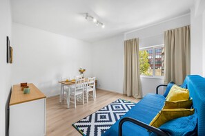 Une pièce moderne et bien éclairée, comprenant un coin repas, un canapé et une fenêtre avec des rideaux.