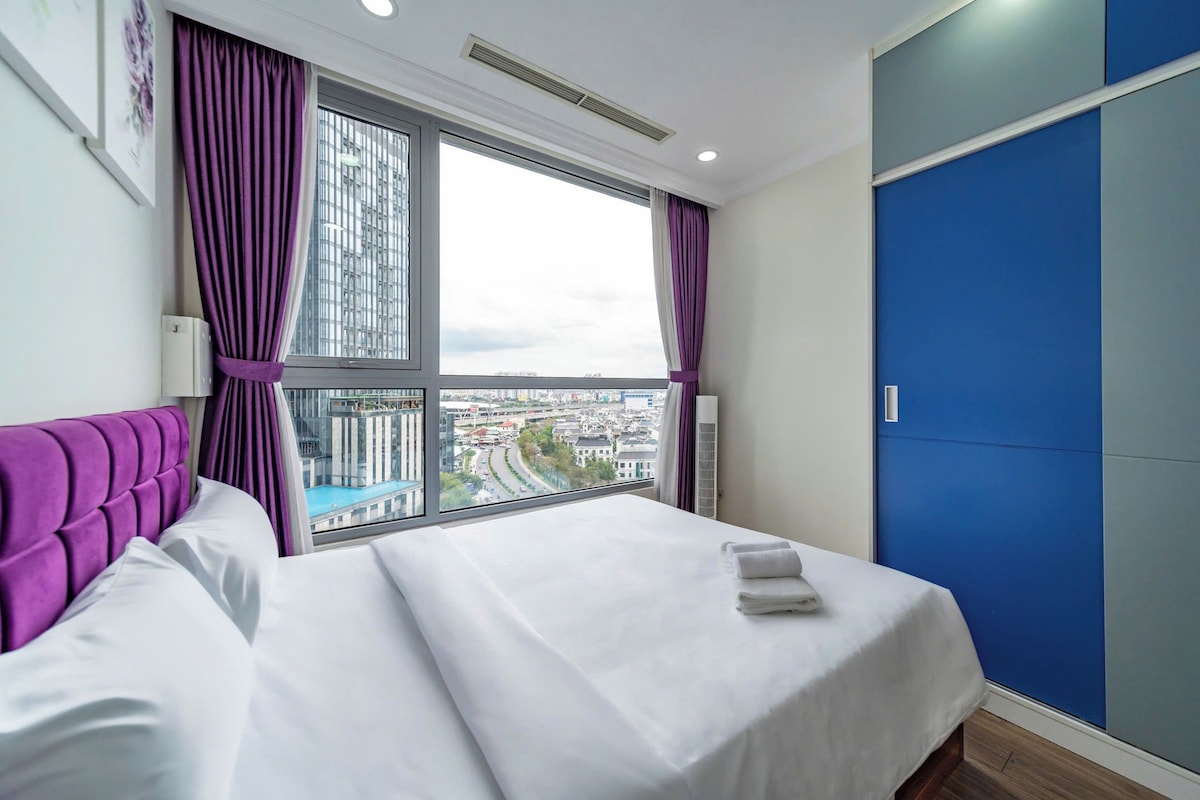 Ein Hotelzimmer mit einem Bett, einem fensterbelaubten Fenster, Blick auf eine Stadtlandschaft und einer blauen Wand.