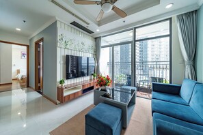 Ein modernes Wohnzimmer mit einem Flachbildfernseher, einem blauen Sofa, einem Couchtisch und einem Balkon mit Blick auf die Stadt.