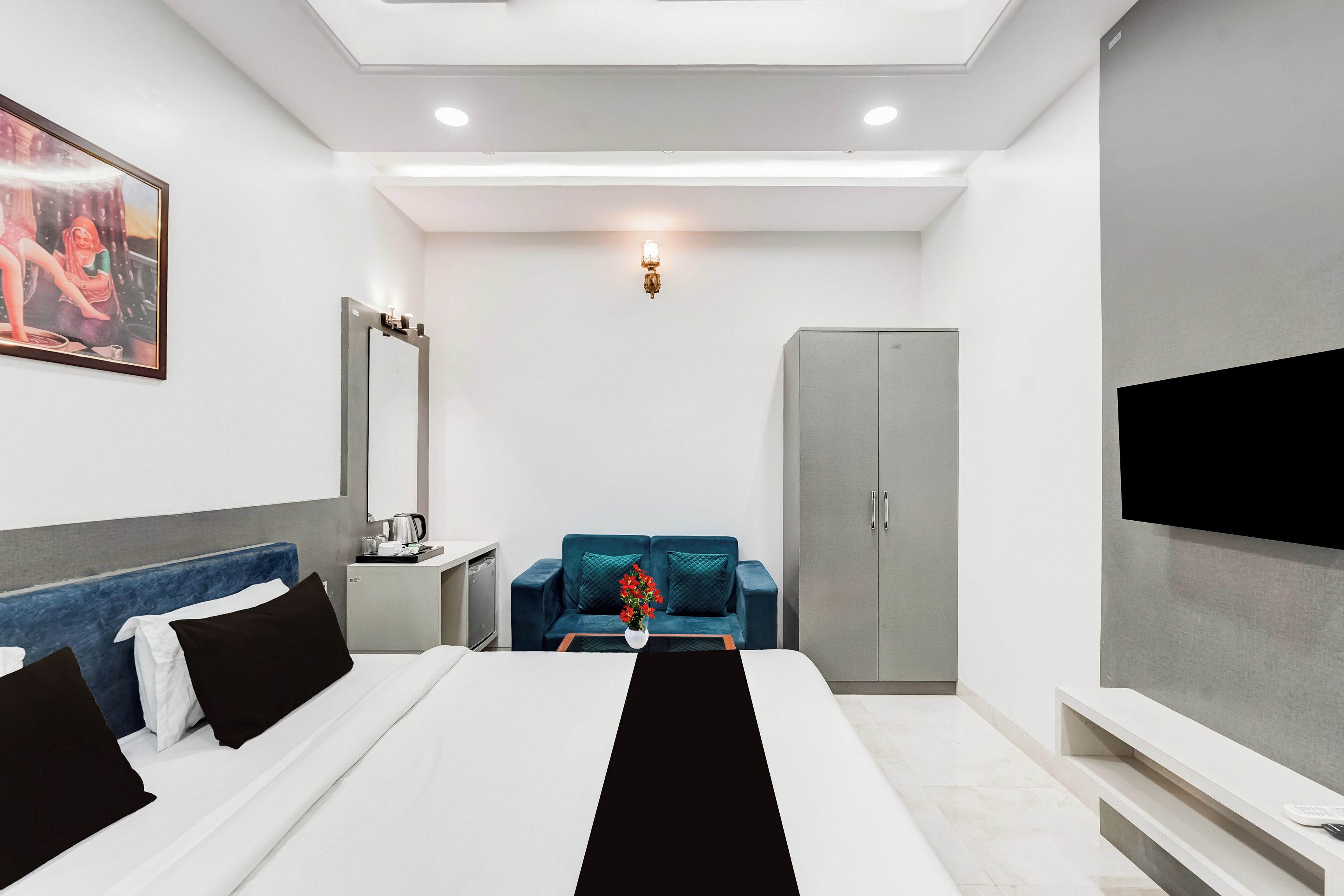 A modern hotel room with a bed, a desk, a sofa, a wardrobe, and a TV.