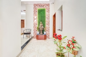 A hallway with a brick wall, a Buddha statue, a wooden chair, and potted plants.