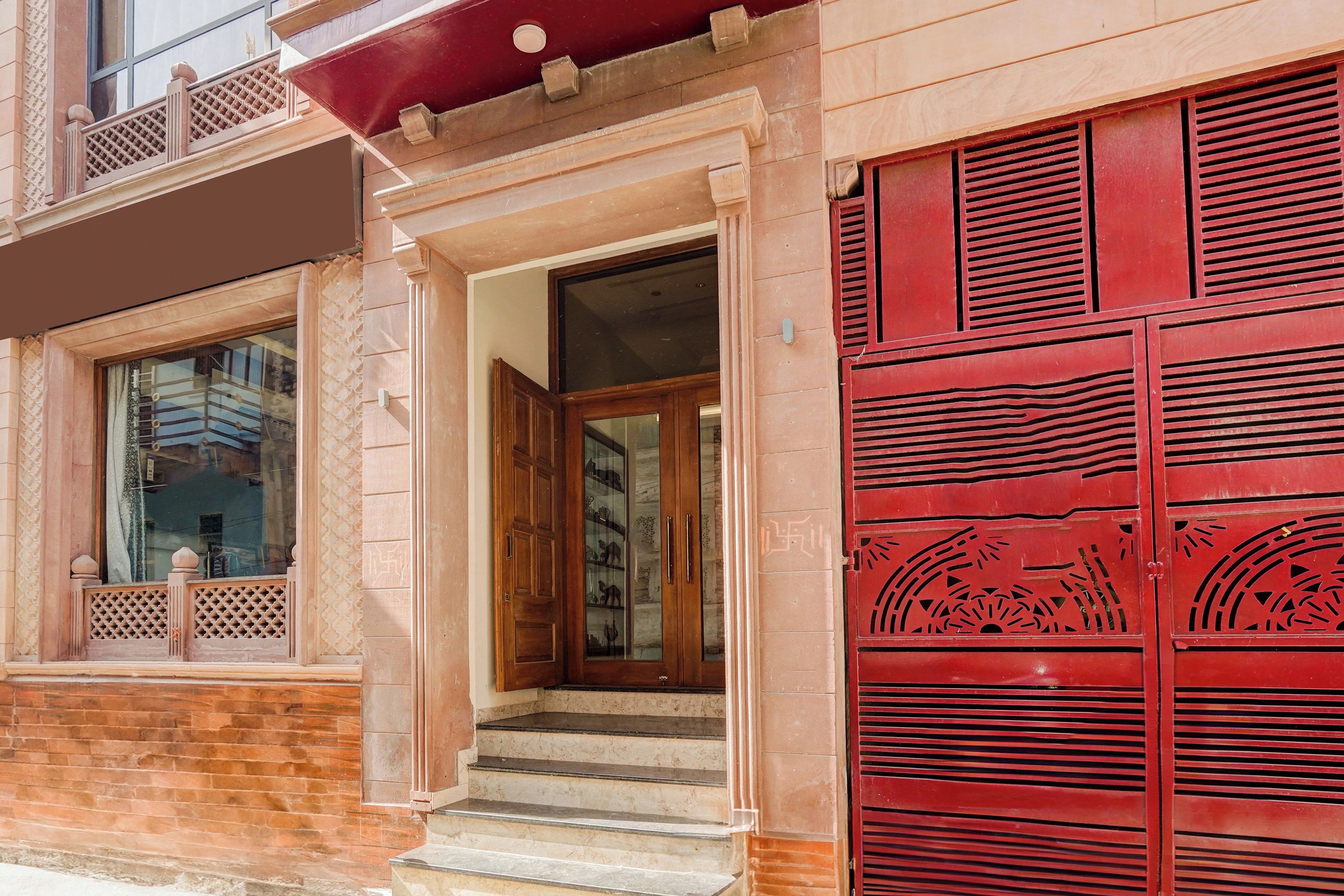 A building entrance with a red door, a set of stairs leading up to the entrance, and a window with a lattice design.