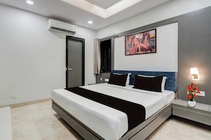 A modern hotel room with a large bed, a flat-screen TV, an air conditioning unit, and a painting on the wall. - Townhouse Jodhpur Clock Tower (Jodhpur)