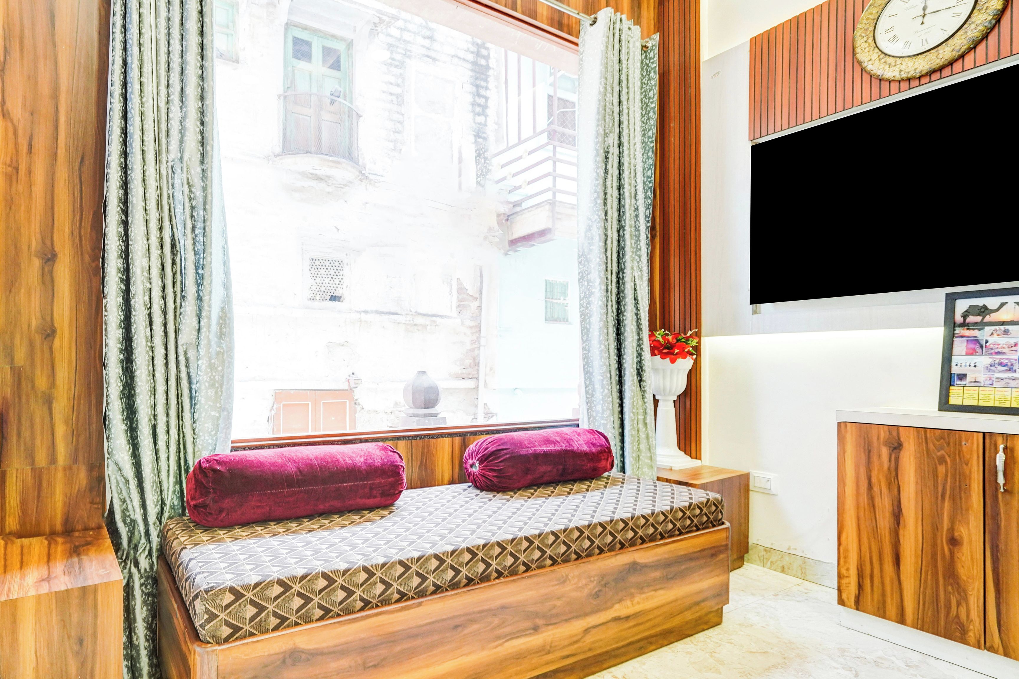 Ein Zimmer mit einer hölzernen Sitzbank, einem an der Wand befestigten Fernseher und einem Fenster mit Vorhängen.