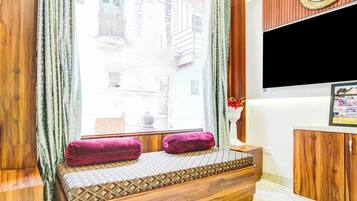 Ein Zimmer mit einer hölzernen Sitzbank, einem an der Wand befestigten Fernseher und einem Fenster mit Vorhängen.