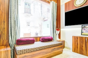 A room with a wooden bench, a TV mounted on the wall, and a window with curtains.