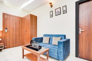 A room with a blue sofa, a wooden wardrobe, a coffee table, and a door.
