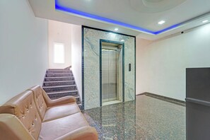 Un vestíbulo con piso de mármol, una sala de espera con sillones de cuero, una escalera y un ascensor.
