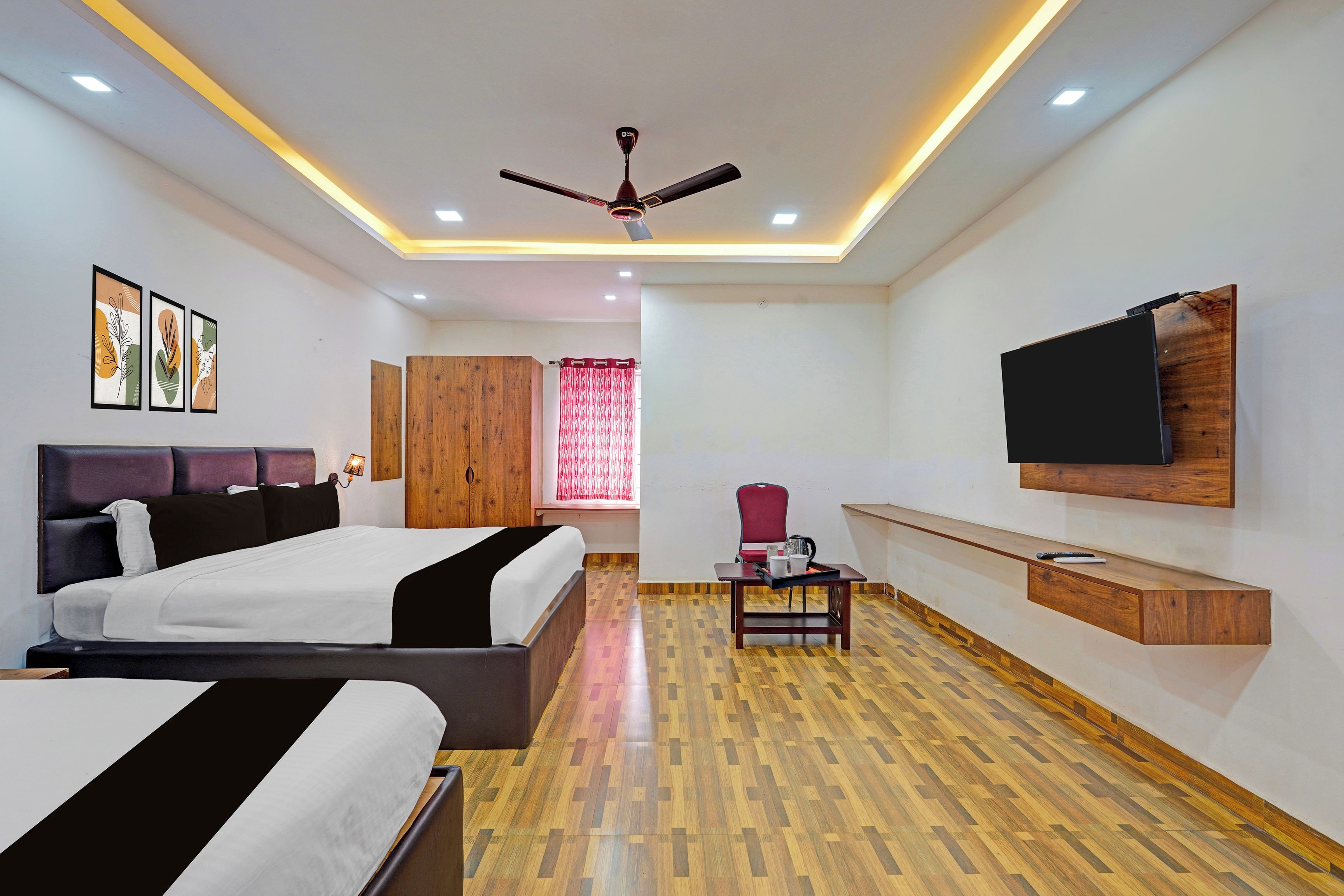 A modern hotel room with a large bed, a desk with a chair, a flat-screen TV mounted on the wall, and a ceiling fan.
