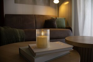 Eine Kerze auf einem Bücherstapel auf einem runden Tisch in einem Raum mit einer Couch und einer Lampe im Hintergrund.