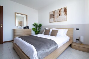 Een moderne slaapkamer met een groot bed, nachtkastjes, een spiegel en kunst aan de muur.