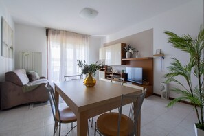 Een woonkamer met een bank, eettafel, stoelen, een televisie en een plant.