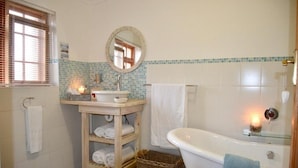 A bathroom with a bathtub, a sink with a mirror, a towel rack, and a wicker basket. - Dassenheuwel Farm Stay Homestead (Malmesbury)