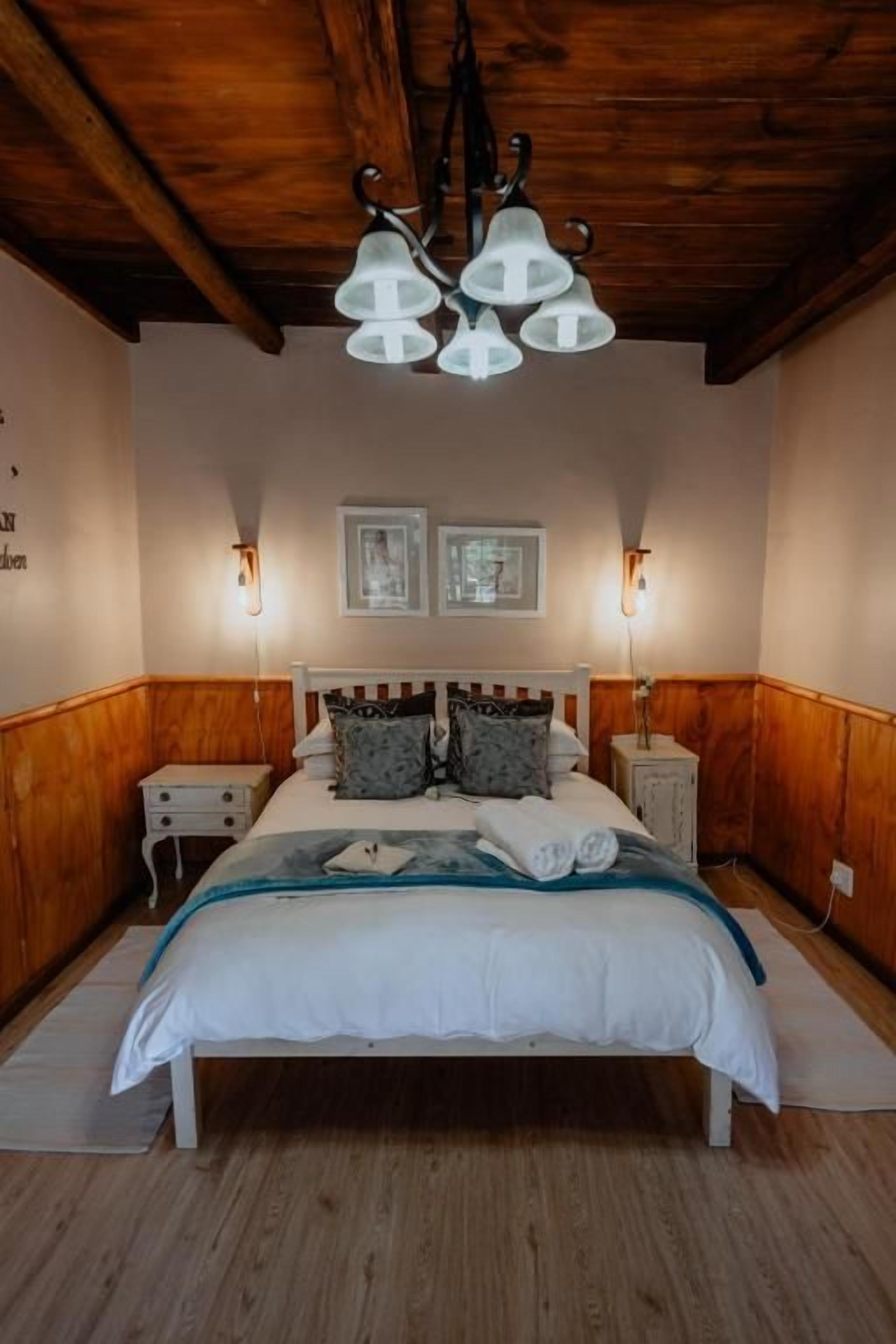 Une chambre avec un plafond en bois, un lit avec une literie blanche, deux tables de chevet et des lampes fixées au mur.